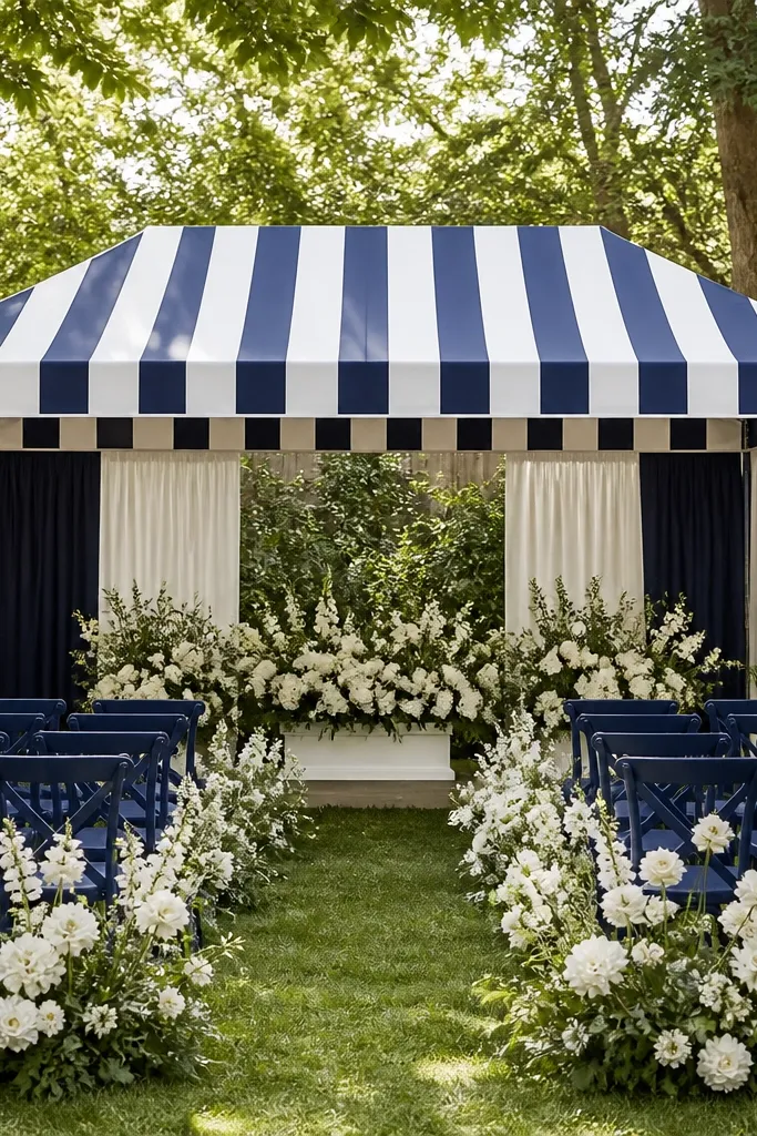 A backyard ceremony tent with navy and ivory striped fabric stretched across a freestanding frame. Clamp-on privacy panels hang on the sides, and the front has a clean straight valance. Navy chairs and white florals sit in front.