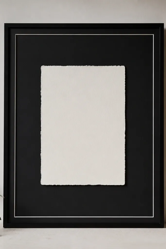 A traditional glass frame with a black mat. A thin white ribbon strip runs along the top and sides like a picture mat. The invitation sits centered in the middle, stark and high-contrast.
