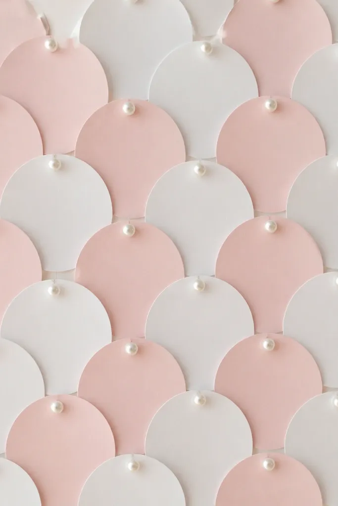 A backdrop made from many cardstock circles in blush and white, pinned in a grid pattern with small pearl pushpins.