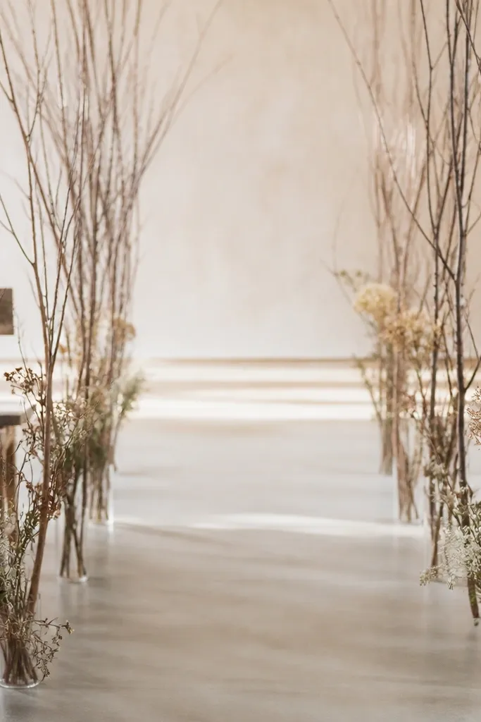 A series of slim twig branches stretched along two sides of an aisle. The branches are tied with floral wire and small clusters of dried flowers sit at intervals.