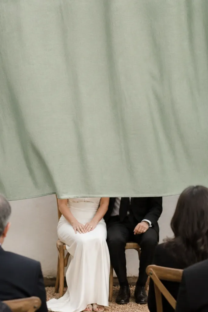 A sage green fabric backdrop hung too low over a small photo area, with the bottom edge cutting across the heads of seated guests in the foreground.