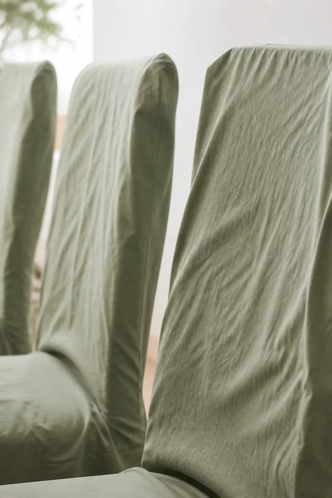 Chair backs with wrinkled sage green fabric covers and uneven draping, visible creases under bright lighting.