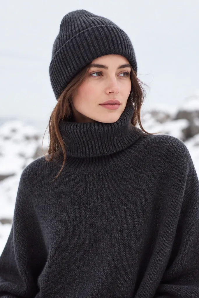 A charcoal turtleneck sweater paired with a matching charcoal knit beanie. The photo shows snowy outdoor light and the outfit looks coordinated.